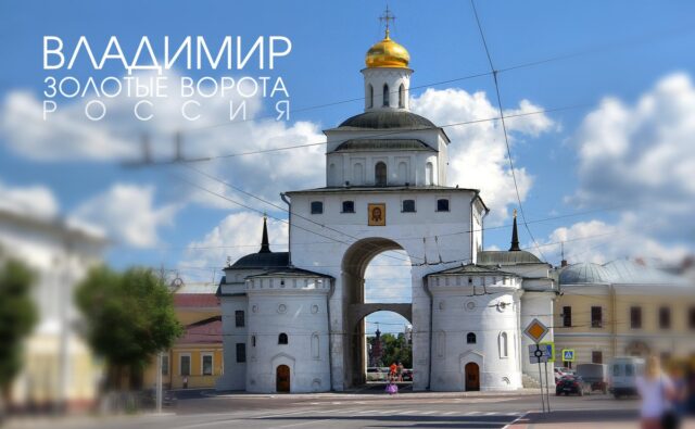 На фотографии изображены Золотые ворота в городе Владимир, Россия. Это историческое сооружение, построенное в белокаменном стиле. В центре композиции находится большая арка, через которую можно пройти. Арка имеет полукруглую форму и поддерживается двумя массивными круглыми башнями по бокам. Над аркой возвышается прямоугольная башня с несколькими окнами. На вершине башни расположен купол с золотым покрытием, увенчанный крестом. Купол имеет форму полусферы и ярко сверкает на солнце. Под куполом, на фасаде башни, находится икона. Башни по бокам арки имеют круглую форму и увенчаны небольшими шпилями. В каждой башне есть несколько окон и дверей. Ворота окружены проводами, которые пересекают изображение в разных направлениях. На переднем плане видна дорога с разметкой и дорожными знаками. Справа от ворот стоит несколько автомобилей и пешеходный переход. На заднем плане, через арку, видны другие здания и деревья. Небо на фотографии ясное, голубое, с небольшими белыми облаками, что придает изображению яркость и контраст. В верхнем левом углу фотографии крупными белыми буквами написано "Владимир Золотые ворота Россия".