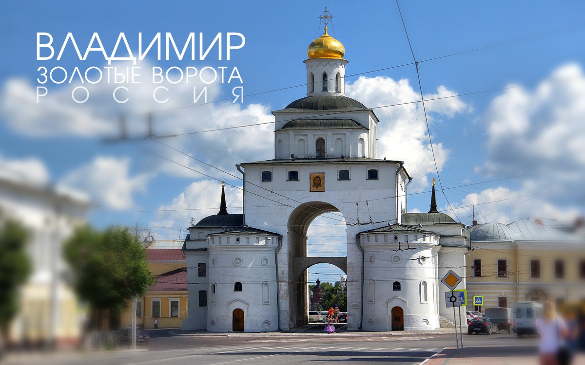 На фотографии изображены Золотые ворота в городе Владимир, Россия. Это историческое сооружение, построенное в белокаменном стиле. В центре композиции находится большая арка, через которую можно пройти. Арка имеет полукруглую форму и поддерживается двумя массивными круглыми башнями по бокам. Над аркой возвышается прямоугольная башня с несколькими окнами. На вершине башни расположен купол с золотым покрытием, увенчанный крестом. Купол имеет форму полусферы и ярко сверкает на солнце. Под куполом, на фасаде башни, находится икона. Башни по бокам арки имеют круглую форму и увенчаны небольшими шпилями. В каждой башне есть несколько окон и дверей. Ворота окружены проводами, которые пересекают изображение в разных направлениях. На переднем плане видна дорога с разметкой и дорожными знаками. Справа от ворот стоит несколько автомобилей и пешеходный переход. На заднем плане, через арку, видны другие здания и деревья. Небо на фотографии ясное, голубое, с небольшими белыми облаками, что придает изображению яркость и контраст. В верхнем левом углу фотографии крупными белыми буквами написано "Владимир Золотые ворота Россия".