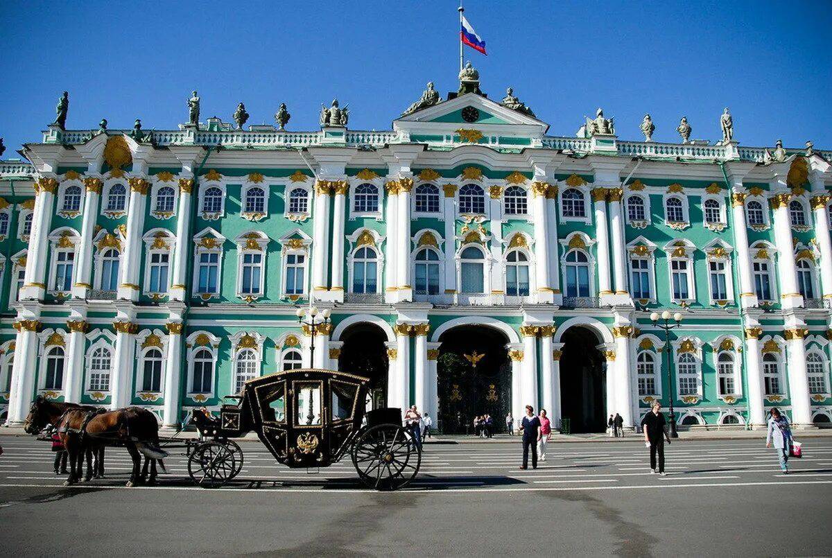 На фотографии изображен Зимний дворец в Санкт-Петербурге, Россия. Это здание имеет три этажа и выполнено в стиле барокко. Стены дворца окрашены в бирюзовый цвет, а окна и колонны выделены белым. Колонны украшены золотыми элементами, которые придают зданию роскошный вид. На крыше дворца расположены статуи, изображающие различных мифологических персонажей. В центре здания находится главный вход, который представлен тремя большими арками. Над центральной аркой виден российский флаг, развевающийся на ветру. Также над арками можно увидеть часы. Перед дворцом на площади стоит черная карета с золотыми украшениями, запряженная двумя лошадьми. Карета имеет классический дизайн с большими колесами и гербом на дверях. Лошади стоят спокойно, а рядом с ними находится человек, вероятно, кучер. На площади перед дворцом ходят люди, некоторые из них фотографируются, другие просто прогуливаются. Погода ясная, небо чистое и голубое, что подчеркивает яркость и красоту здания.