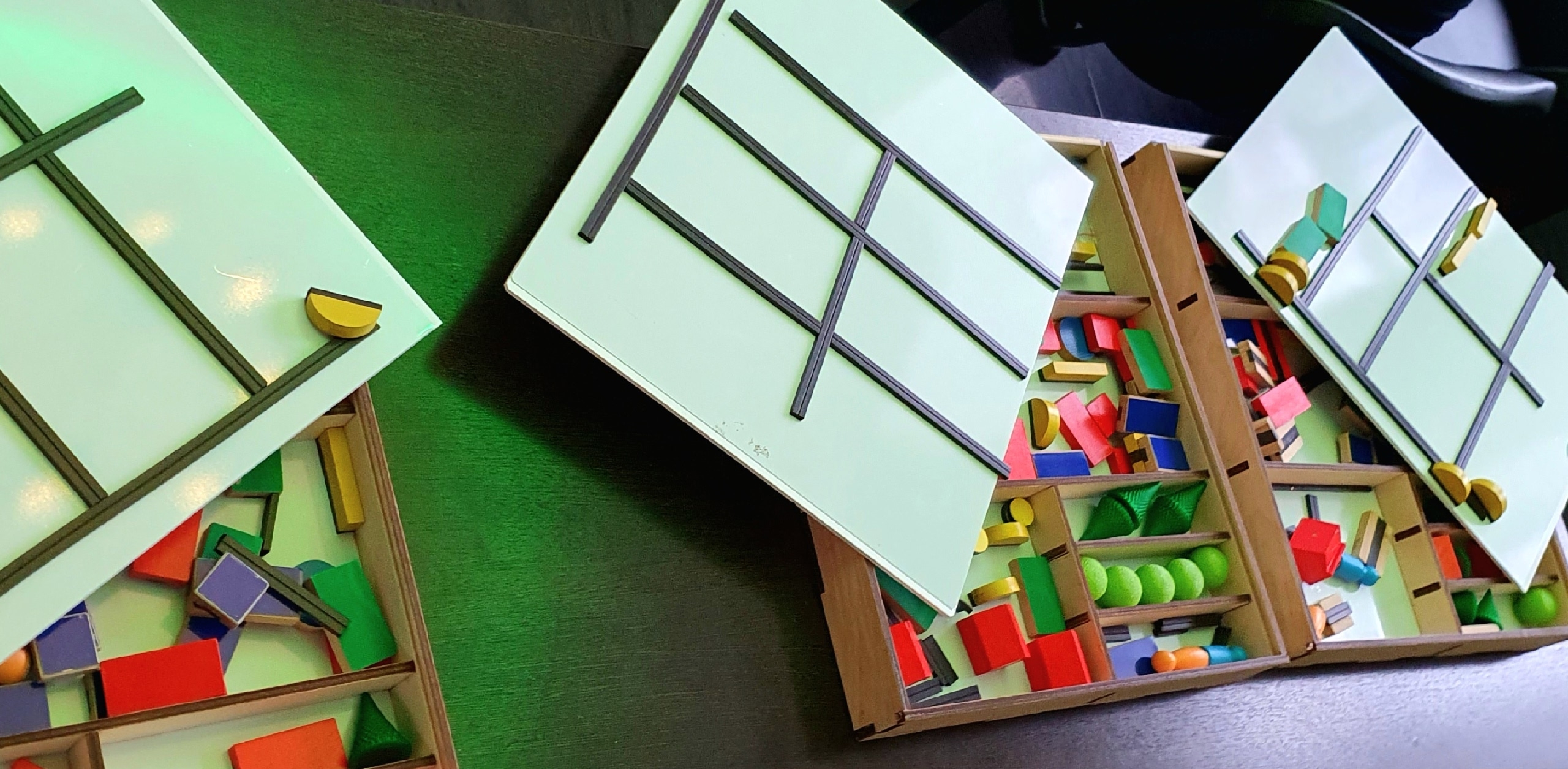 Магнитно-тактильные конструкторы "Ориентир": три коробки, внутри которых находятся различные геометрические фигуры из дерева или пластика — кубики, прямоугольники, полусферы, шары, палочки и другие цветные элементы. На белых магнитных крышках размещены черные пересекающиеся линии.